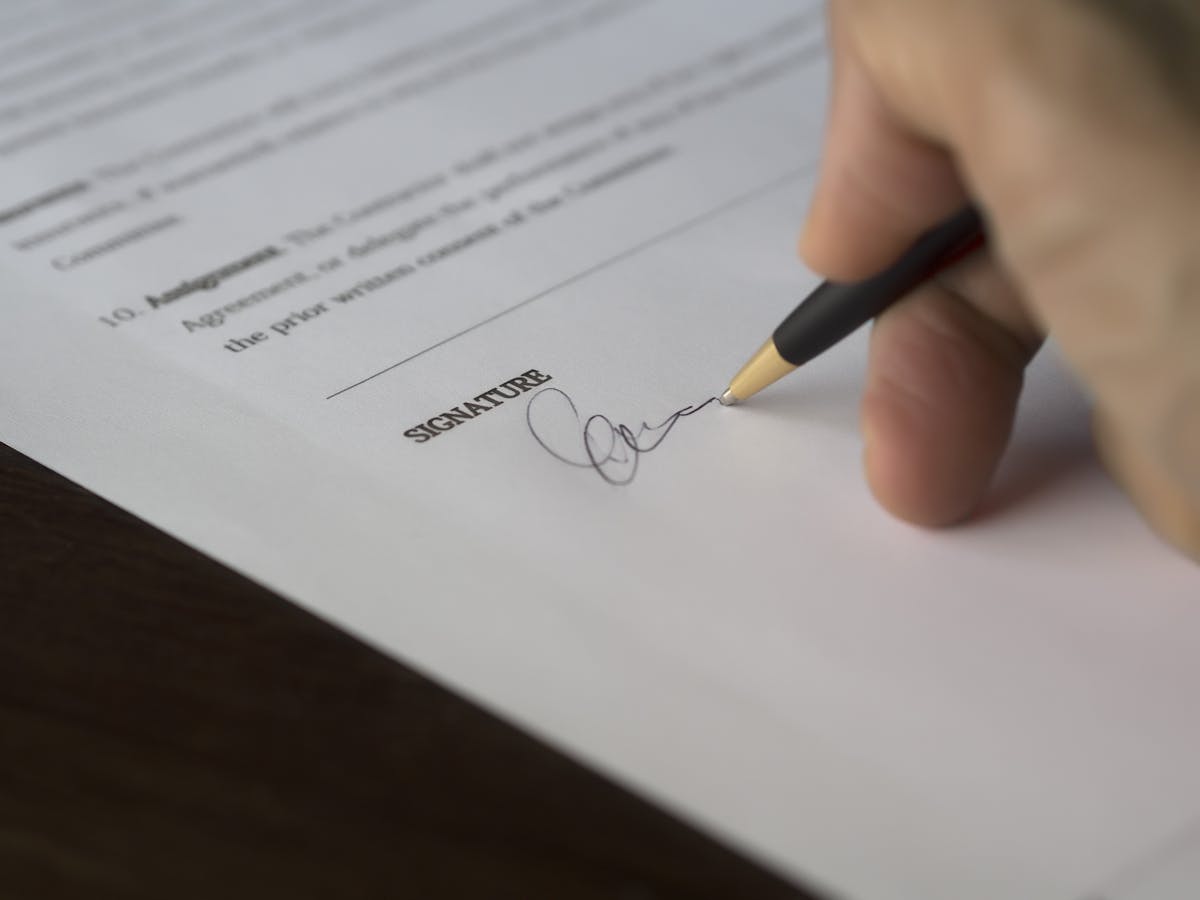 Close-up of a hand signing a formal document on a wooden desk