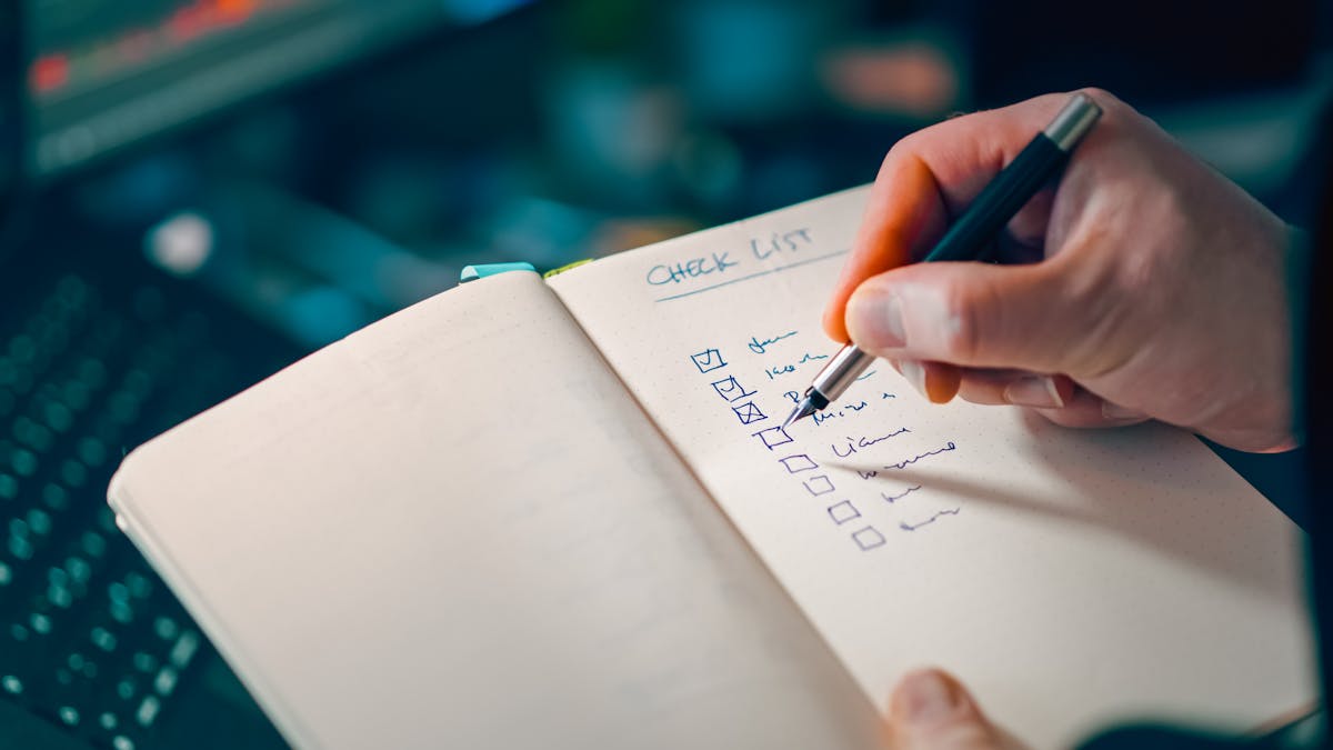 Personne écrivant une checklist dans un carnet pour la gestion des tâches